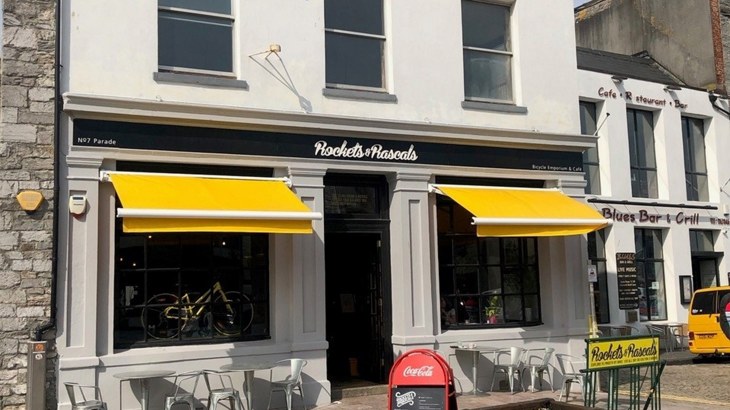 Facade of cafe with yellow outdoor shades over the windows and a bike in one of the windows