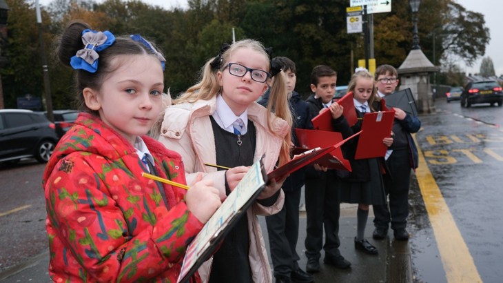 Children observing traffic and taking notes outside of school