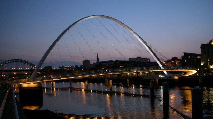 Modern pedestrian bridge with lights underneath, over river in city at night