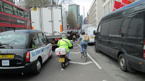 A person on a bicycle tries to navigate through congestion in London