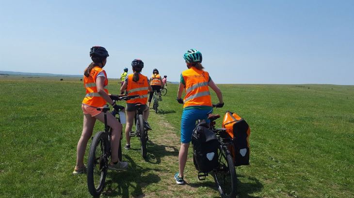 girls on bikes in Walk Wheel Cycle Trust hivis on a grass hill with blue skies