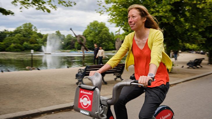 Woman cycles past Victoria Park in Hackney on a city hire bike.