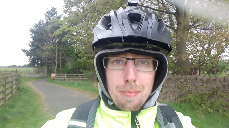 Man wearing glasses, hood, black cycling helmet and high-vis jacket on cycle path
