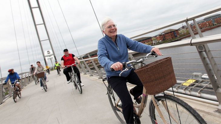 Elderly lady riding her bike over a bridge