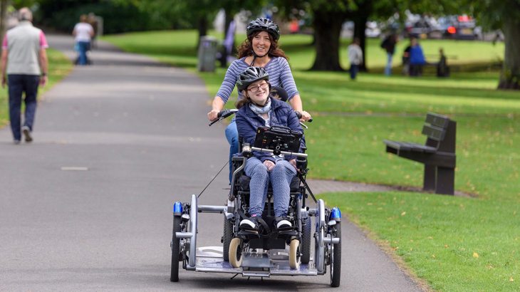Mum and child cycling through park on an adapted trailer bike