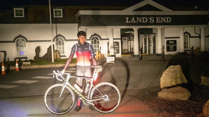 Tom standing with his bike and helmet in front of Lands End at 4am in the morning