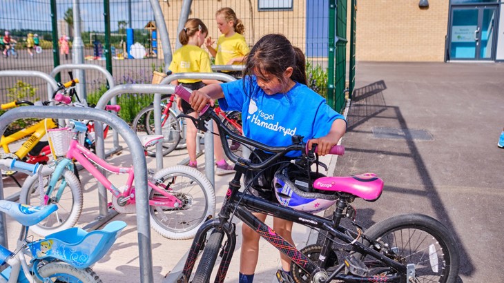 A girl in a blue t-shirt locking her bike to a Sheffield cycle stand in the school playground