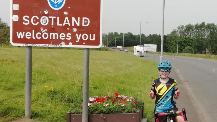 boy on bike next to Scotland sign