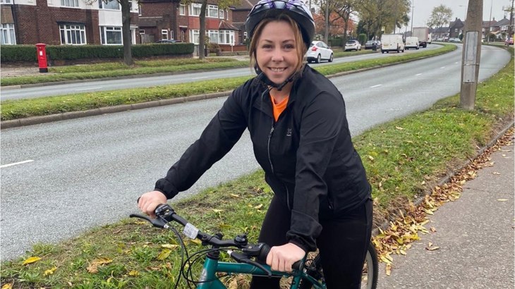 Liverpool Labour Councillor, Sharon Connor, standing with her bike on a residential paved street wearing a helmet and a black waterproof jacket.