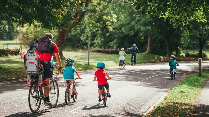 a family with young children ride their bicycles through a park on a sunny day