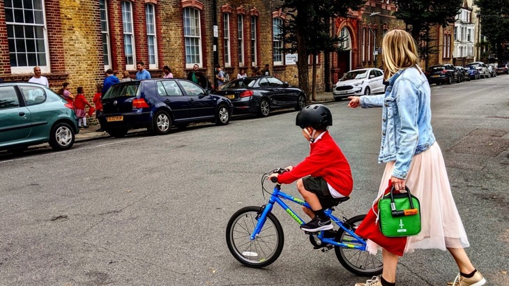 Child in school uniform on bike on road outside school