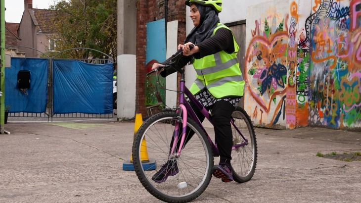 Woman in high vis vest cycles in a car park