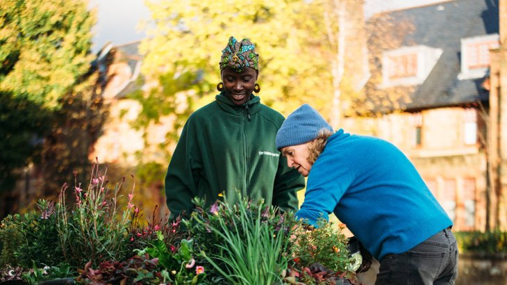 Two women chatting, planting flowers in a street planter on their road.