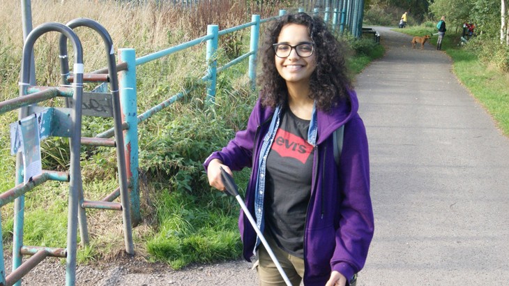 A girl smiling on a traffic-free route using a litter picker to collect rubbish and clear the route.