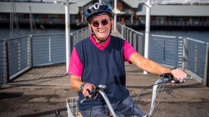 Man wearing sunglasses and a cycle helmet, sitting on his tricycle smiling and laughing.