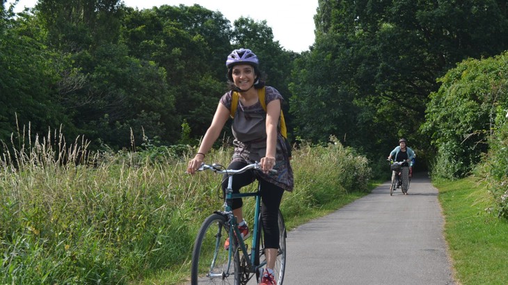 Our West Midlands partnerships manager, Ridhi Kalaria cycling along a traffic-free path in England, wearing her helmet and smiling.