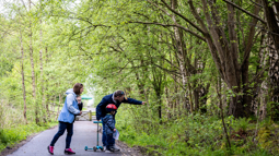 A family of three with a young child on a scooter on a traffic-free path surrounded by greenery the man is pointing towards a hedge 